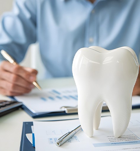Man in blue shirt calculating invoice at desk next to large model tooth