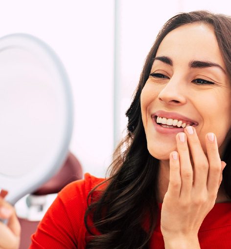 Woman in red-orange shirt smiling at her reflection in a handheld mirror