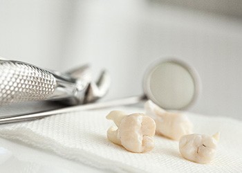 Three extracted teeth on gauze next to dental instruments