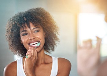 Woman in white tank top at bathroom sink brushing teeth