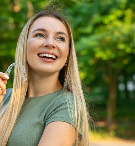Smiling woman holding CandidPro clear aligner