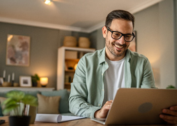 Man with glasses smiling while working on laptop at home