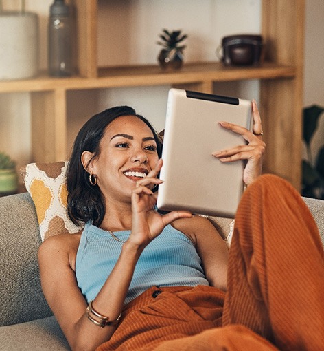 Smiling woman looking at tablet while relaxing on couch