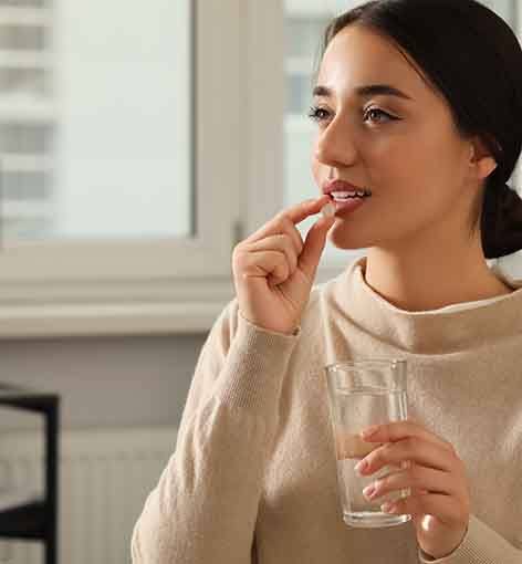 Woman in beige sweater taking a pill with a glass of water