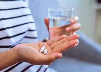 Hands holding two pills and a glass of water