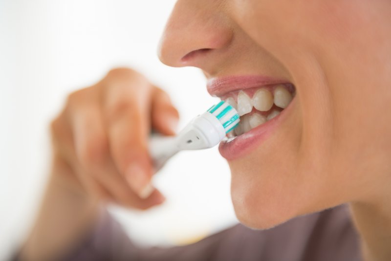 A closeup of a woman brushing her teeth too hard